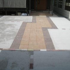 カーポートから玄関へと続くアプローチには、落ち着いた色合いの30ｃｍ角の平板（コンクリート製舗装材）を使用しています。コンクリートの目地にはインターロッキング（コンクリート製舗装材）をランダムに多色使用しています。
