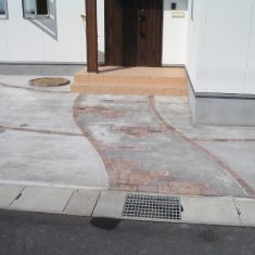 駐車スペースとアプローチは土間コンクリートですが、目地は２色使用のランダム配置で表情をつけています。玄関横には植栽用のサークルを設けています。