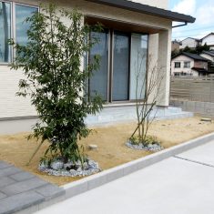 お家の奥側には敷地の境界としてブロックの上にＹＫＫＡＰの「シンプレオフェンスＳＹ１型」を設置しています。<br />
シンボルツリーの足元には和石を敷き、下草を植えているため華やかな印象になります。